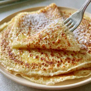 Close-up of a fork lifting a translucent French crepe showing its flexible and lacy texture with buttery sheen.