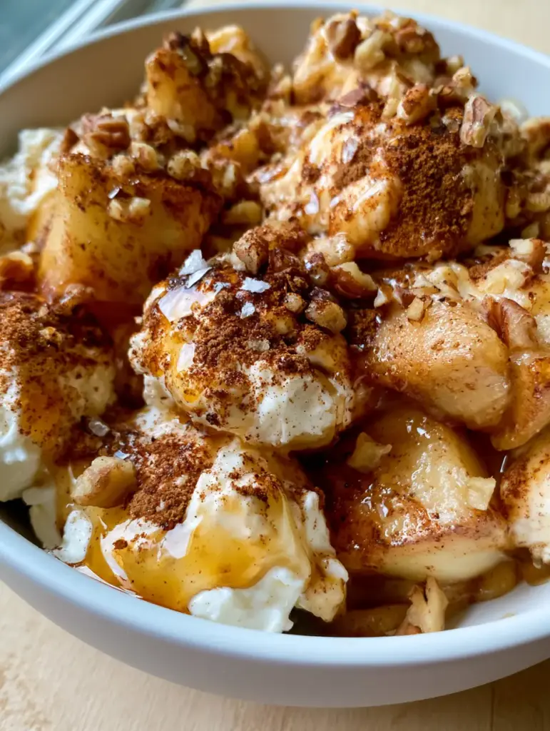 Bird's eye view of a bowl of Cinnamon Apple Cottage Cheese Bites with glistening maple syrup and crushed pecans.