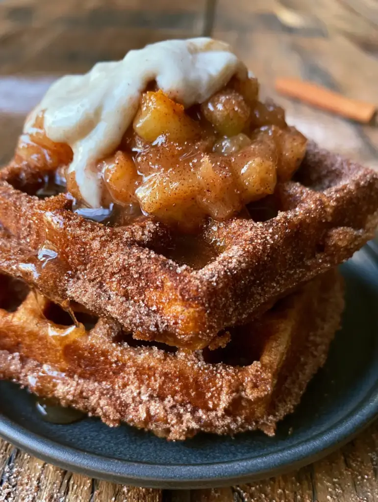 A stack of two thick churro apple pie waffles with amber-colored Granny Smith apple chunks and translucent cinnamon syrup.