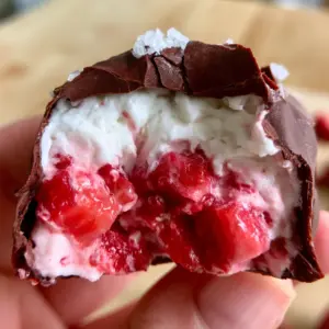 A close-up of a frozen strawberry chocolate cluster with a matte finish and a visible 'crack' from a bite. (frozen strawberry chocolate)